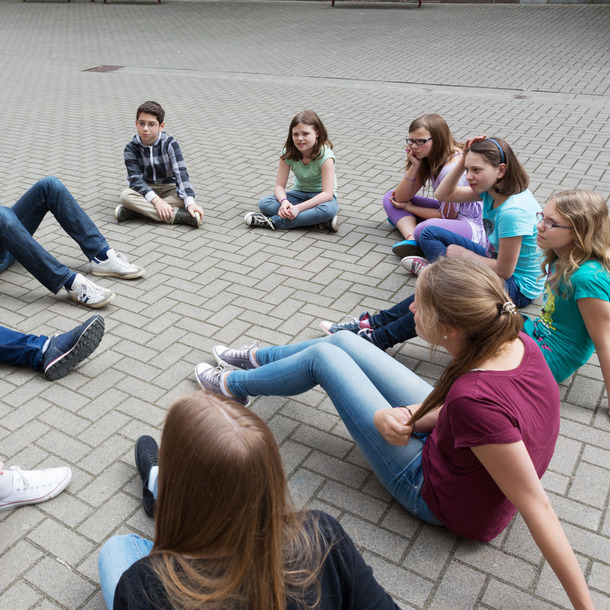 [Translate to English:] Kinder und Jugendliche sitzen im Kreis auf dem Boden und unterhalten sich
